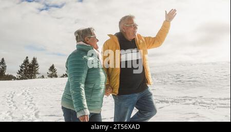 Felice coppia anziana che cammina insieme attraverso la neve durante l'inverno - concetto di stile di vita per persone anziane gioiose - concentrazione morbida sul viso dell'uomo Foto Stock