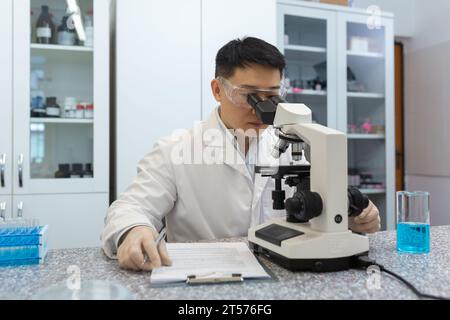 Giovane scienziato maschio asiatico, medico che lavora in laboratorio al microscopio, studiando e ricercando con concentrazione. Foto Stock