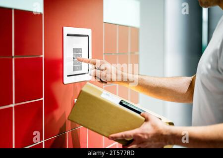 Armadietto per pacchi. Servizio pacchi. Box e telefono cellulare. Uomo che usa il codice per ritirare la consegna. Terminal delle spedizioni presso l'ufficio postale. Foto Stock