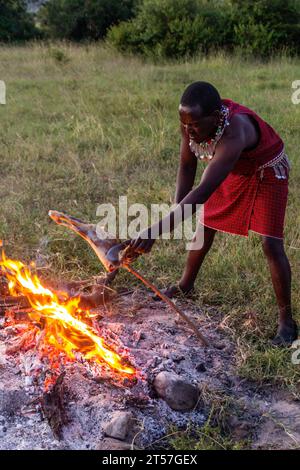 MASAI MARA, KENYA - 20 FEBBRAIO 2020: Uomo Masai che tosta una gamba di capra, Kenya Foto Stock