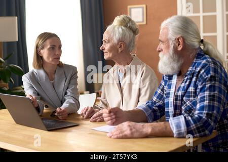 Consulente finanziario che utilizza il laptop e parla con la coppia senior durante l'incontro a casa Foto Stock