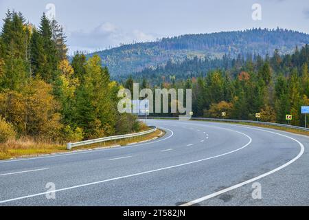 Imbarcati in un pittoresco viaggio lungo una vecchia strada asfaltata che si snoda attraverso un'affascinante foresta autunnale gialla. Le vivaci tonalità del fogliame Foto Stock