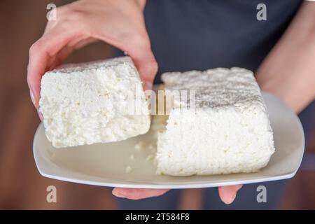 Le mani tengono il formaggio cottage da vicino. Mettere il formaggio cottage sul tavolo. Concetto di alimentazione sana. Foto Stock