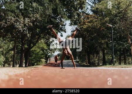 Persona maschile elastica che pratica cardio e flessibilità nel parco, con ruote in cartoncino per ottenere risultati positivi. Foto Stock