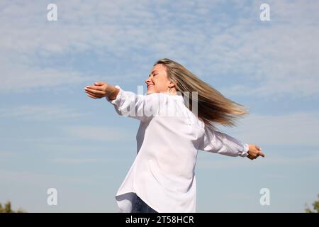 ESPRESSIONI DI FELICITÀ E BENESSERE DA UNA RAGAZZA BIONDA IN CAMICIA BIANCA CON CIELO BLU SULLO SFONDO Foto Stock