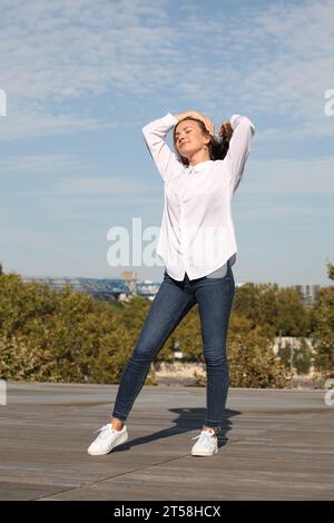 ESPRESSIONI DI FELICITÀ E BENESSERE DA UNA RAGAZZA BIONDA IN CAMICIA BIANCA CON CIELO BLU SULLO SFONDO Foto Stock