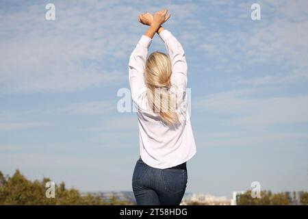 ESPRESSIONI DI FELICITÀ E BENESSERE DA UNA RAGAZZA BIONDA IN CAMICIA BIANCA CON CIELO BLU SULLO SFONDO Foto Stock