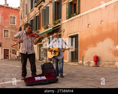 Un violinista sorridente e chitarrista che suona in una piazza pubblica di Venezia. La custodia per chitarra è aperta e vediamo due CD. Foto Stock