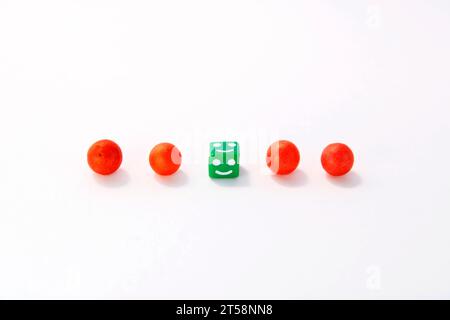 Fila di sfere rosse e cubo verde al centro con un'espressione facciale che fa la differenza Foto Stock