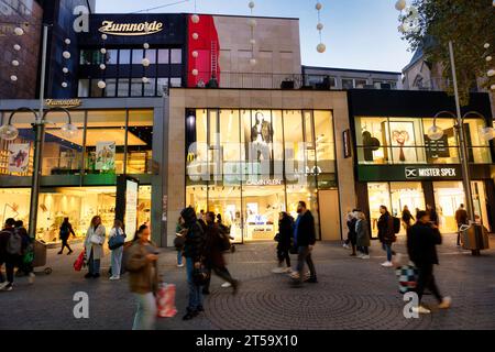 Colonia, Germania 03 novembre 2023: Pedoni di fronte ai negozi illuminati al crepuscolo sulla famosa via dello shopping schildergasse a colonia Foto Stock