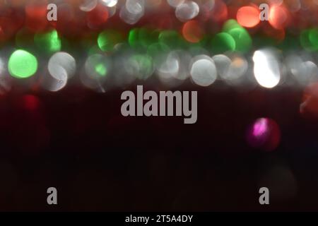 Luce riflessa da file di tinsel dai colori vivaci, creando un design bokeh astratto sulla parte superiore dell'immagine. Spazio nero sul lato inferiore. Foto Stock