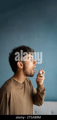 L'uomo arabo che spruzza la medicina in bocca, disinfettando nel suo orale, prevenzione dell'infezione respiratoria. Concetto di assistenza sanitaria. Foto Stock