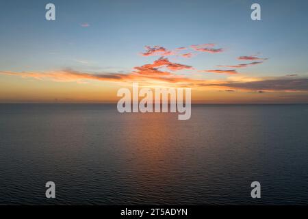 Spettacolare cielo rosso luminoso al tramonto sull'oceano, tenui nuvole serali sull'acqua scura del mare Foto Stock