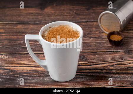 La cannella spruzzò il salep in una tazza bianca sul tavolo di legno Foto Stock