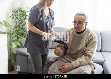 Giovane infermiera sorridente che prende la pressione sanguigna del vecchio Foto Stock