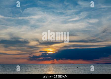 Raggi crepuscolari che si infrangono nella copertura delle nuvole e una striscia dorata di luce solare che attraversa il canale Foto Stock