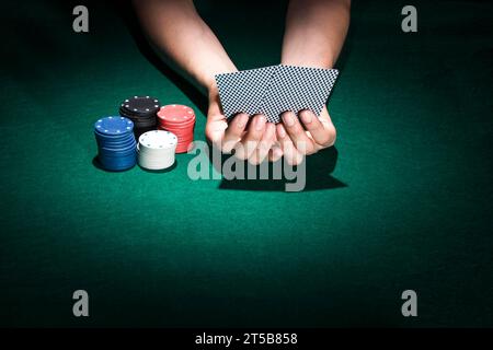 Persona che tiene la mano della carta da gioco con il tavolo del casinò con gettoni da poker impilabili Foto Stock