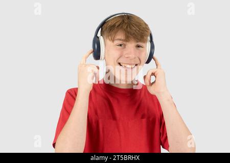 Un ragazzo di 15 anni felice e sorridente, che indossa una t-shirt rossa e ascolta musica con le cuffie Foto Stock