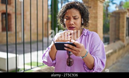 Giovane bella donna latina che guarda un video sullo smartphone che sembra sconvolta per strada Foto Stock