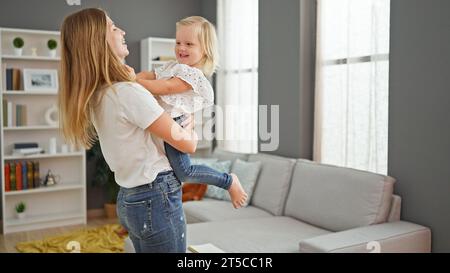 Madre allegra che tiene in braccio la figlia sorridente, in piedi nella loro accogliente casa Foto Stock