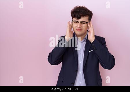Giovane uomo non binario con barba che indossa tuta e cravatta con mano sulla testa per dolore alla testa a causa dello stress. soffre di emicrania. Foto Stock