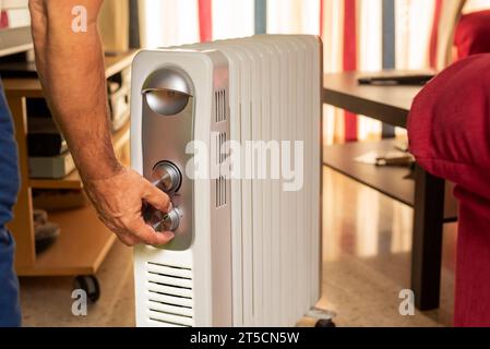 Mano dell'uomo che seleziona la temperatura su un radiatore domestico in salotto. Foto Stock
