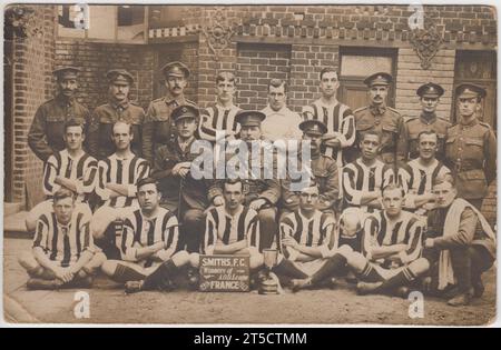 Smiths FC, vincitori della Army Ordnance Department (AOD) League, Francia, 1916/7: Fotografia di squadra di una squadra di calcio dell'esercito della prima guerra mondiale. Mostra un gruppo di uomini, alcuni in divisa da calcio, altri in uniforme dell'esercito, in posa con una coppa fuori da un edificio in mattoni leggermente danneggiato. Uno dei giocatori (fila centrale, seconda da destra) è di origine africana o caraibica, un altro soldato (fila superiore, estrema sinistra) può anche essere di origine non europea Foto Stock