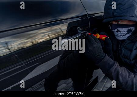 Ho tentato di rubare un'auto usando una valigia in centro - un ladro in un cappuccio con una maschera sul viso Foto Stock