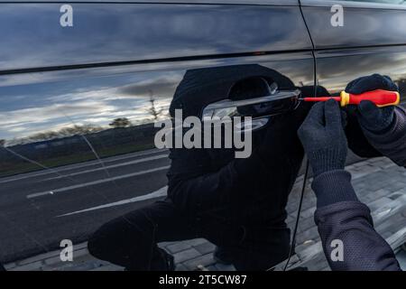 Ho tentato di rubare un'auto usando una valigia in centro - un ladro in un cappuccio con una maschera sul viso Foto Stock