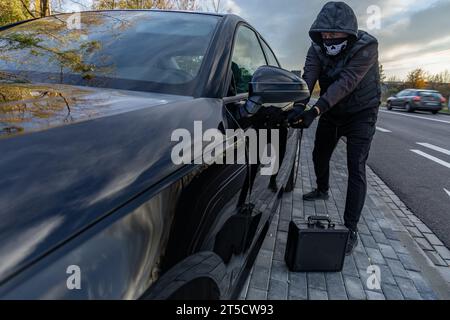 Ho tentato di rubare un'auto usando una valigia in centro - un ladro in un cappuccio con una maschera sul viso Foto Stock