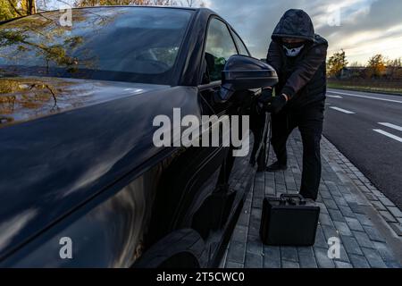 Ho tentato di rubare un'auto usando una valigia in centro - un ladro in un cappuccio con una maschera sul viso Foto Stock