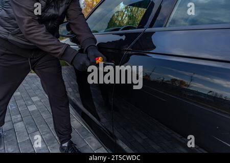 Ho tentato di rubare un'auto usando una valigia in centro - un ladro in un cappuccio con una maschera sul viso Foto Stock