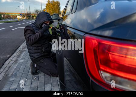 Ho tentato di rubare un'auto usando una valigia in centro - un ladro in un cappuccio con una maschera sul viso Foto Stock