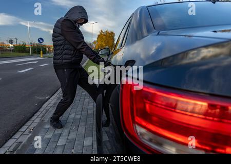 Ho tentato di rubare un'auto usando una valigia in centro - un ladro in un cappuccio con una maschera sul viso Foto Stock