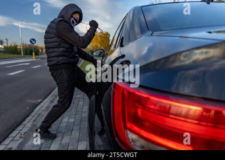 Ho tentato di rubare un'auto usando una valigia in centro - un ladro in un cappuccio con una maschera sul viso Foto Stock