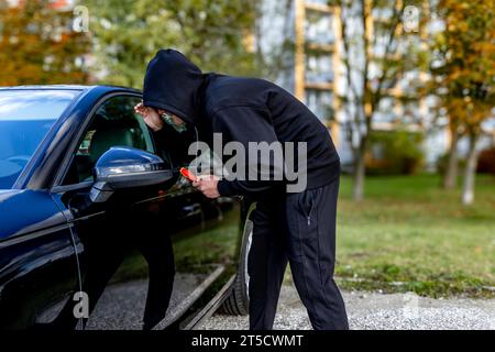 Ho tentato di rubare un'auto usando una valigia in centro - un ladro in un cappuccio con una maschera sul viso Foto Stock