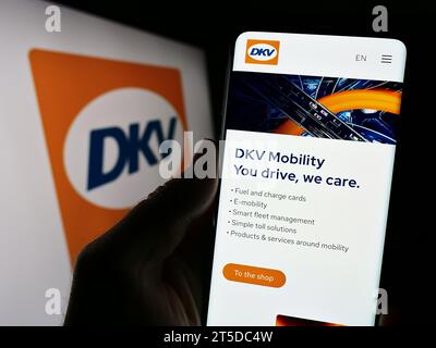 Persona che possiede il cellulare con la pagina Web dell'azienda tedesca di pagamenti B2B DKV Mobility davanti al logo aziendale. Concentrarsi sul centro del display del telefono. Foto Stock