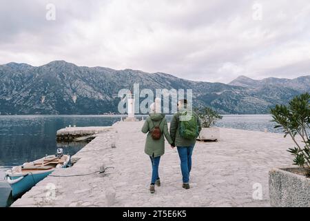 I due camminano lungo il molo verso il faro, tenendosi per mano. Vista posteriore Foto Stock