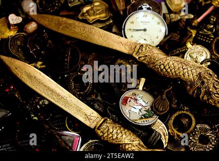 Un'antica corona di zecca reale, coniata durante il regno della regina Vittoria, smaltata in sette colori, si trova tra gli amuleti religiosi protettivi buddisti con due coltelli metallici che brillano su entrambi i lati. L'orologio da tasca di un vecchio gentiluomo è fuori fuoco e mostra le 08,44 del mattino. Foto Stock