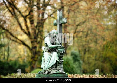 una figura funeraria femminile siede in lutto ai piedi di una croce con un'urna su uno sfondo autunnale sfocato Foto Stock