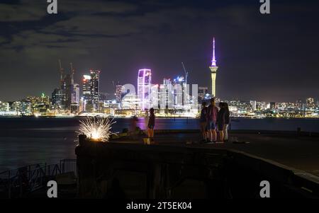 Sky Tower illuminata di rosa e giallo per celebrare Diwali. Famiglia e amici illuminano fuochi d'artificio per Guy Fawkes. Auckland. Foto Stock