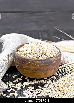 Scritto in una ciotola e sul tavolo, steli con orecchie di grano, un tovagliolo da rapa sullo sfondo di una tavola di legno nera Foto Stock