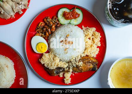 Nasi Lemak su un piatto rosso con condimenti e bevande. Vista orizzontale o superiore. Cibo tipico malese. Sfondo bianco isolato. Foto Stock