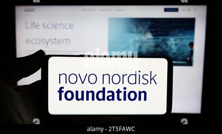 Persona che possiede uno smartphone con il logo dell'organizzazione danese Novo Nordisk Foundation davanti al sito Web. Concentrarsi sul display del telefono. Foto Stock