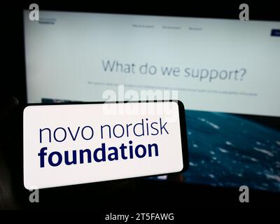 Persona che possiede il cellulare con il logo dell'organizzazione danese Novo Nordisk Foundation davanti alla pagina Web. Concentrarsi sul display del telefono. Foto Stock