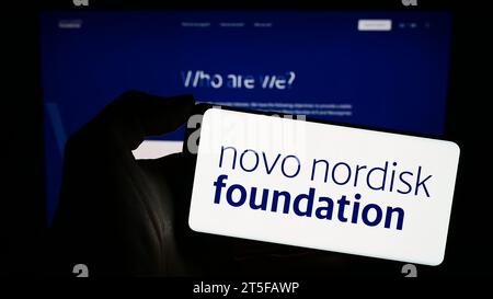 Persona che possiede un telefono cellulare con il logo dell'organizzazione danese Novo Nordisk Foundation davanti alla pagina Web. Concentrarsi sul display del telefono. Foto Stock