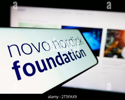 Smartphone con logo dell'organizzazione danese Novo Nordisk Foundation davanti al sito Web. Mettere a fuoco il display centrale sinistro del telefono. Foto Stock