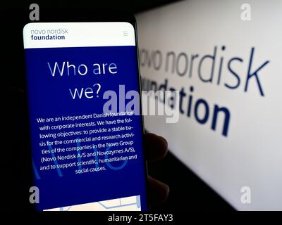 Persona che possiede uno smartphone con una pagina Web dell'organizzazione danese Novo Nordisk Foundation davanti al logo. Concentrarsi sul centro del display del telefono. Foto Stock