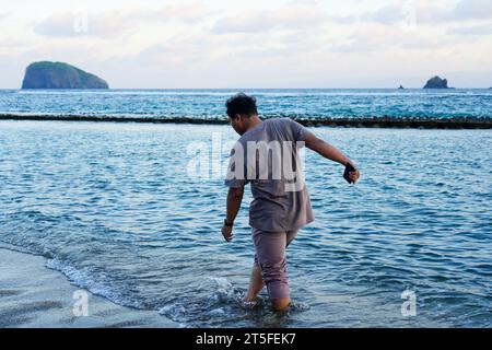 un uomo cammina tranquillamente sulla spiaggia, assaporando la melodia rilassante delle onde dell'oceano. Passeggiate in spiaggia Foto Stock