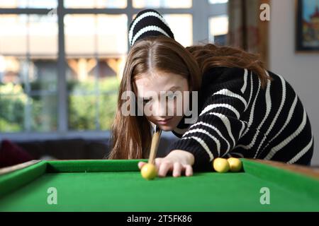 Teen girl che gioca al tradizionale gioco da pub di bagatelle nella lounge di casa, in fila per un tiro con un segnale Foto Stock